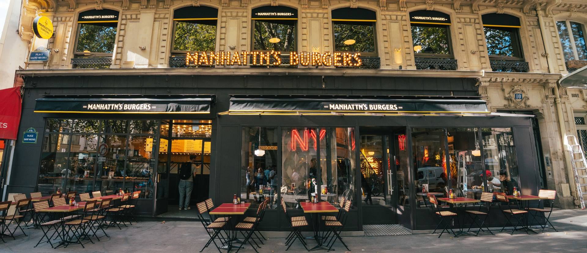 La devanture de Manhattn's Burgers place Saint-Michel, ses enseignes lumineuses et sa terrasse