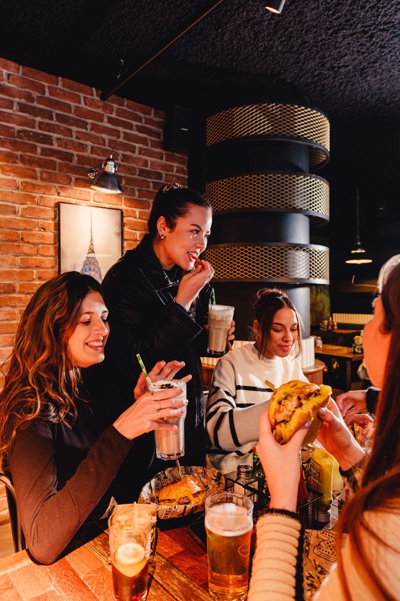 Une tablée d'amies devant leurs burgers, contre un mur de briques rouges